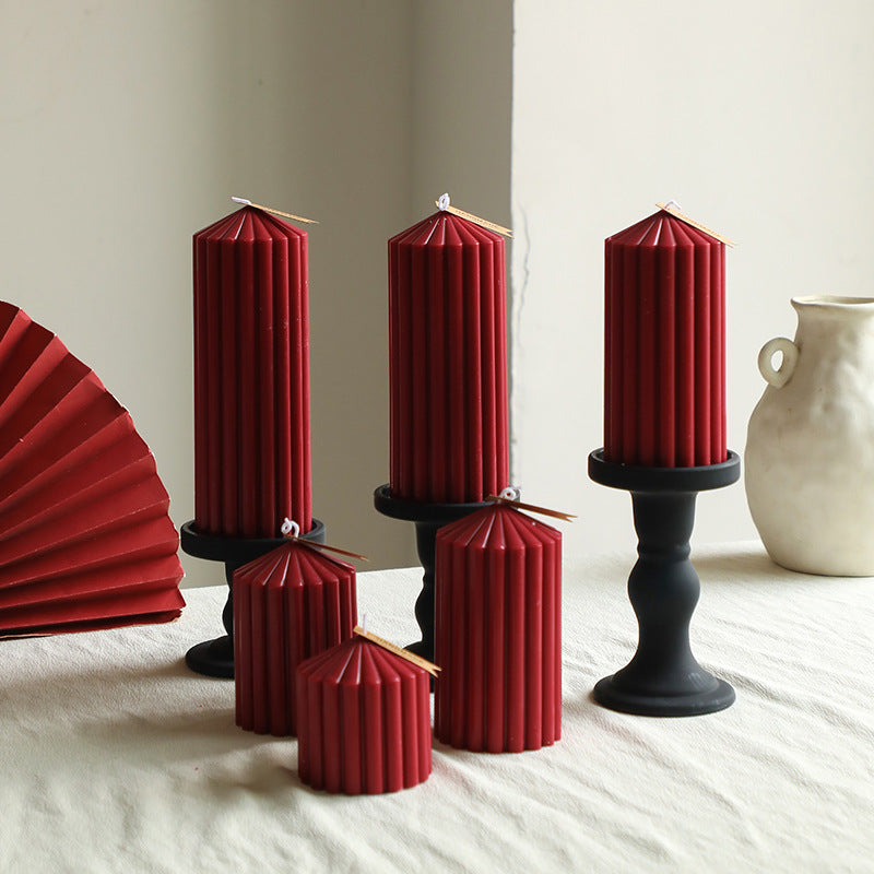 Set of red folded candles on black stands with a white vase in the background.