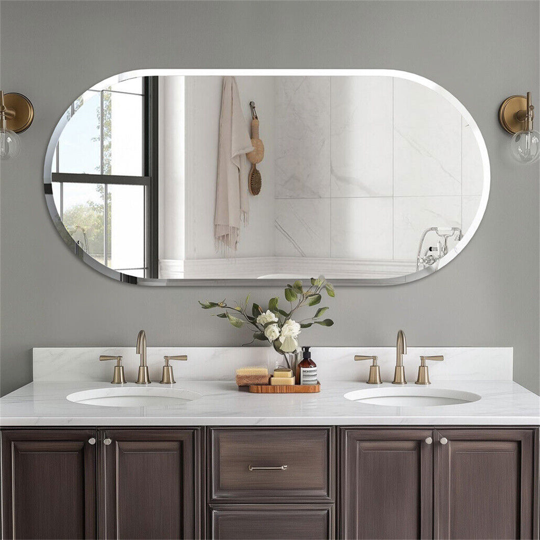 An oval wall-mounted bathroom mirror with a white frame, mounted on a gray wall above a double-sink vanity with dark wood cabinets and brass faucets.