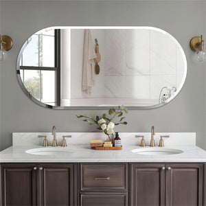 An oval wall-mounted bathroom mirror with a white frame, mounted on a gray wall above a double-sink vanity with dark wood cabinets and brass faucets.