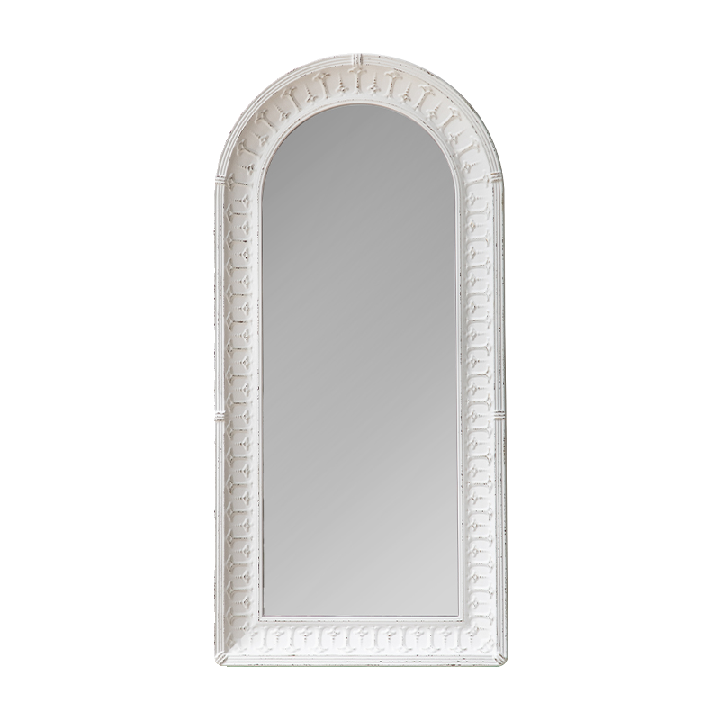 An arched wall mirror with a distressed white frame featuring decorative carved details around the border.